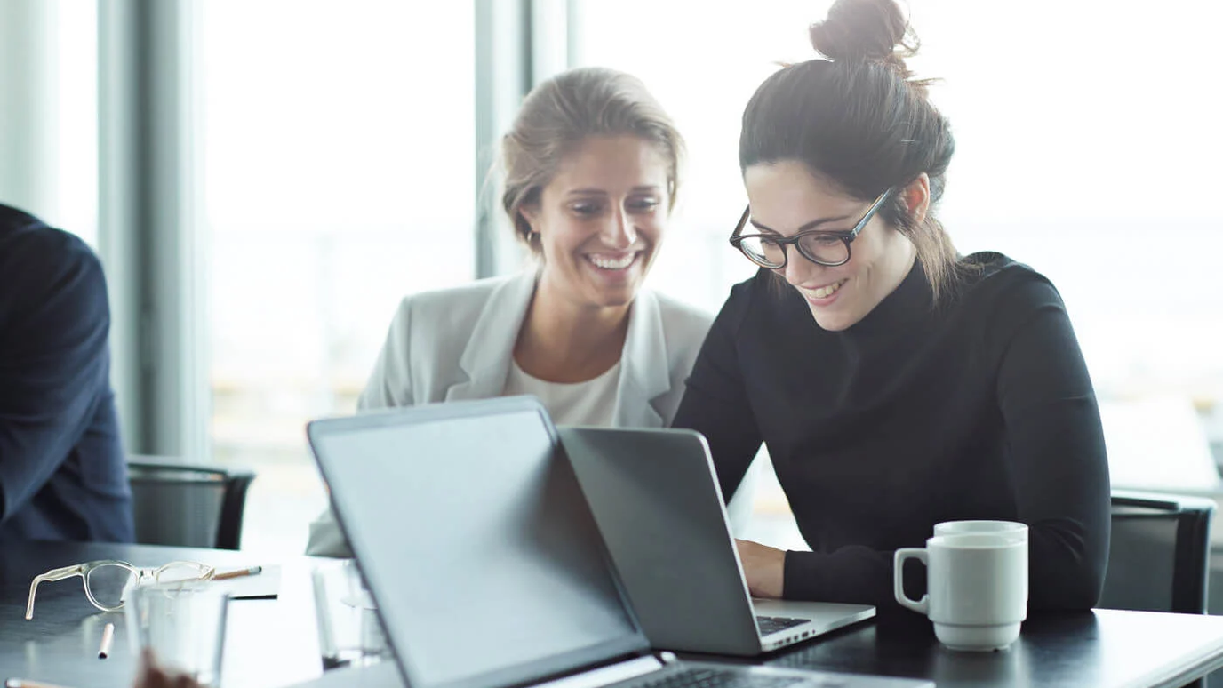 Two colleagues smiling at a laptop in an office